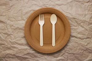 Wooden fork, spoon on cardboard plate on crumpled paper background photo