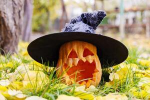 Víspera de Todos los Santos calabaza en bruja sombrero en amarillo hojas en el parque o bosque en otoño foto