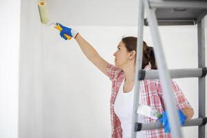 mujer con pintar rodillo y cepillo en escalera pintura paredes en su Departamento foto