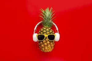 Ripe pineapple with sunglasses and headphones on red background photo