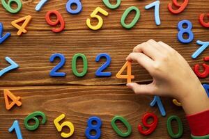Child makes up the year 2024 from multicolored numbers on a wooden background photo