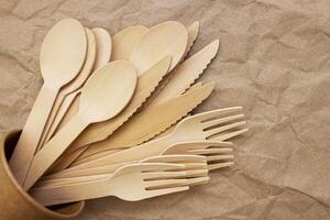 Wooden forks, spoons and knifes in cardboard cup on crumpled paper photo