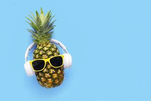 Ripe pineapple with sunglasses and headphones on blue background photo