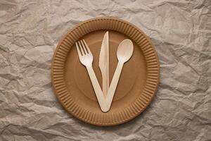 Wooden fork, spoon and knife on cardboard plate on crumpled paper photo