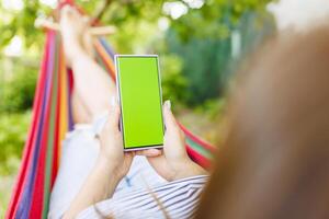 Woman lying on hammock in garden ,she holds smartphone in hands with a chromakey photo