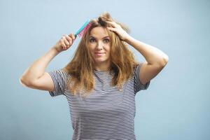 Upset young woman looking with shock at her damaged hair on blue background photo