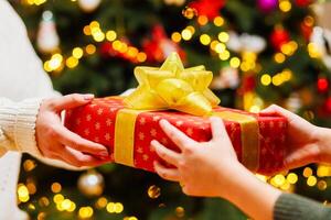 Hands of parent giving Christmas gift to child on Christmas tree background photo