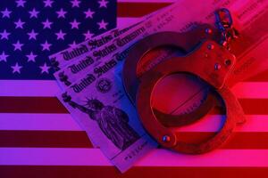 US Tax refund check and handcuffs on flag of United States of America close up photo