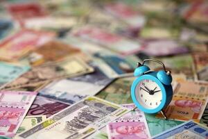 Small alarm clock on many banknotes of different currency. Background of time and money photo