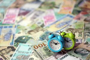 pequeño alarma reloj en muchos billetes de diferente divisa. antecedentes de hora y dinero foto
