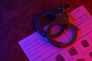 Applicant or fingerprints card with police handcuffs on table in dark room photo
