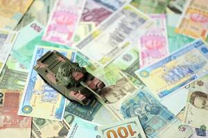 Small green tank on many banknotes of different currency. Background of war funding photo