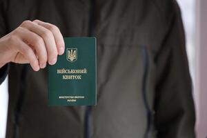 Young ukrainian conscript soldier shows his military token or army ID ticket indoors photo