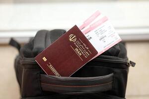 Red Islamic Republic of Iran passport with airline tickets on touristic backpack photo