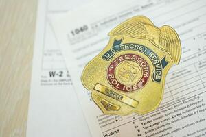 KYIV, UKRAINE - MARCH 9, 2024 US Treasury Police Secret Service Officer badge on 1040 and W-2 IRS tax forms photo