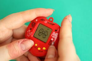 KYIV, UKRAINE - MARCH 9, 2024 Retro pet keychain game tamagotchi in red plastic case in female hands photo