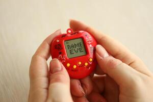 KYIV, UKRAINE - MARCH 9, 2024 Retro pet keychain game tamagotchi in red plastic case in female hands photo