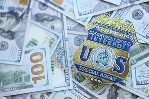 KYIV, UKRAINE - MARCH 9, 2024 US Interpol Special Agent badge on many US hundred dollar bills photo