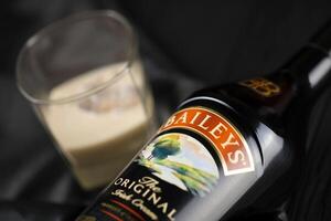 KYIV, UKRAINE - MAY 4, 2022 Baileys original alcohol bottle on wooden table with black fabric photo