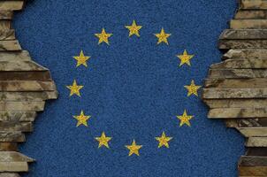 European union flag depicted in paint colors on old stone wall closeup. Textured banner on rock wall background photo