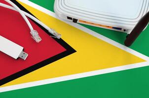 Guyana flag depicted on table with internet rj45 cable, wireless usb wifi adapter and router. Internet connection concept photo