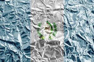 Guatemala flag depicted in paint colors on shiny crumpled aluminium foil closeup. Textured banner on rough background photo
