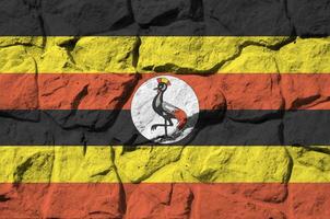 Uganda flag depicted in paint colors on old stone wall closeup. Textured banner on rock wall background photo