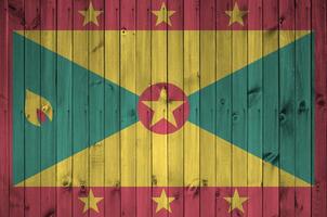Grenada flag depicted in bright paint colors on old wooden wall. Textured banner on rough background photo