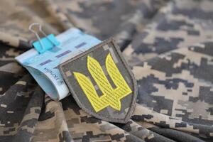 Ukrainian army symbol and bunch of hryvnia bills on military uniform. Payments to soldiers of the Ukrainian army, salaries to the military photo