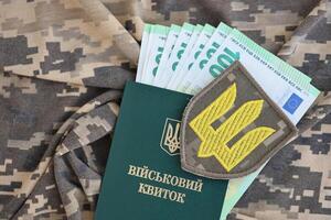 Symbol of Ukrainian army and military ID with bunch of money on the camouflage uniform of a Ukrainian soldier. Concept of payment to military personnel or bribe for deferment from service photo