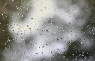 una foto de gotas de lluvia en el cristal de la ventana con una vista borrosa de los árboles verdes florecientes. imagen abstracta que muestra las condiciones meteorológicas nubladas y lluviosas