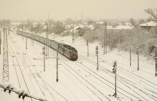 A long train of passenger cars is moving along the railway track. Railway landscape in winter after snowfall photo