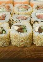 Close-up of a lot of sushi rolls with different fillings lie on a wooden surface. Macro shot of cooked classic Japanese food with a copy space photo