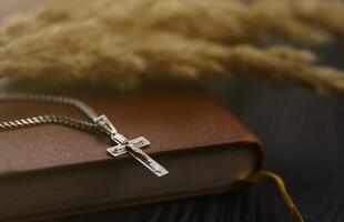 Silver necklace with crucifix cross on christian holy bible book on black wooden table. Asking blessings from God with the power of holiness photo