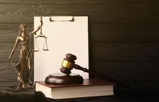 Lady justice or justitia the Roman goddess of Justice. Statue on brown book with judge gavel on blank paper background with copyspace. Concept of judicial trial, courtroom process and lawyers work photo