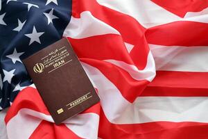 Red Islamic Republic of Iran passport on United States national flag background close up photo