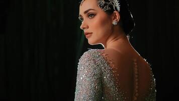 Elegant woman in a sparkling evening gown with a backless design, posing against a dark background. video