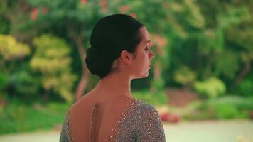 Rear view of a woman with a bun hairstyle looking to the side, standing outdoors with greenery video