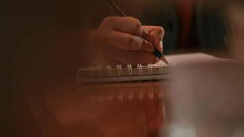 Close-up of a person's hand writing in a notebook on a wooden table with a blurred foreground. video