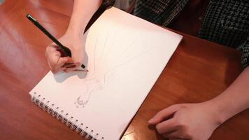 Close-up of a person sketching in a notebook on a wooden table, creative concept. video