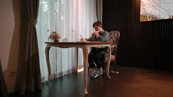 Man writing in notebook at a vintage desk with sheer curtains and soft lighting in the background. video