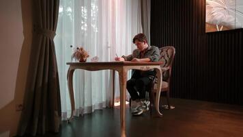 Man writing in notebook at home with small dog watching, natural light from window. video