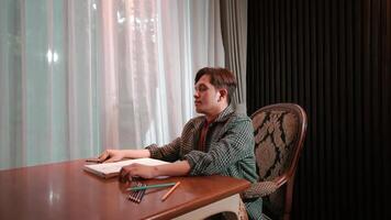 Stressed man at desk with head in hands, feeling overwhelmed with work, with book and pen in front of him. video