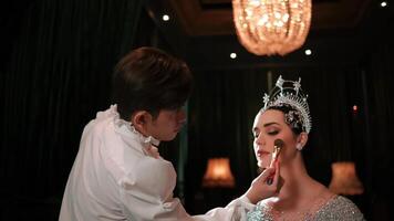 Makeup artist applying cosmetics to a woman in an elegant dress with a tiara, preparing for an event. video