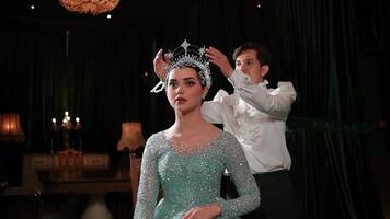 Elegant couple performing a dance, woman in a sparkling dress and tiara, man in a white shirt, dark backdrop. video