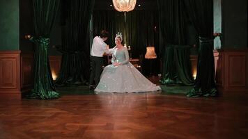 Elegant couple dancing in a ballroom, woman in a tiara and gown, man in a suit, romantic setting with dark backdrop. video