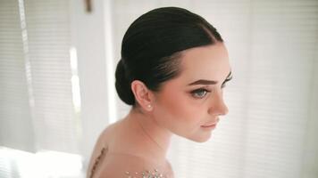 Elegant woman with a bun hairstyle by the window, soft light creating a serene atmosphere. video