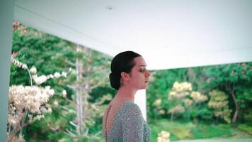 lado perfil do uma contemplativo mulher em pé dentro de casa com uma jardim Visão através a janela. video