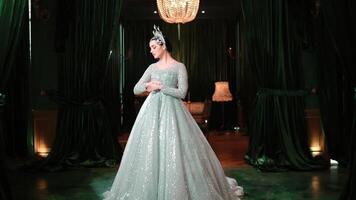 Elegant woman in a sparkling evening gown standing in a luxurious room with dark curtains and a chandelier. video