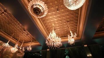 Elegant chandeliers hanging from a decorative ceiling with intricate patterns, casting a warm glow. video